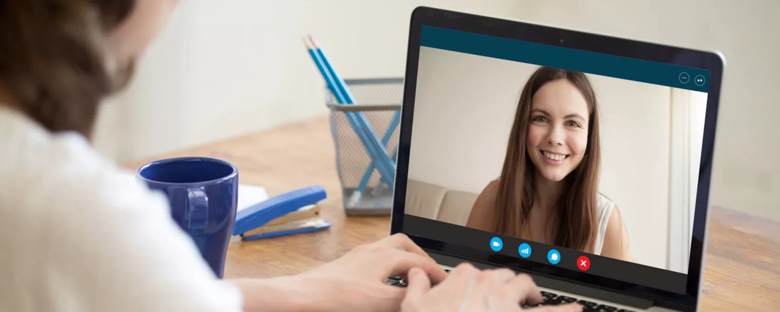 A woman on a laptop screen smiles as someone types on the keyboard and views the monitor. 