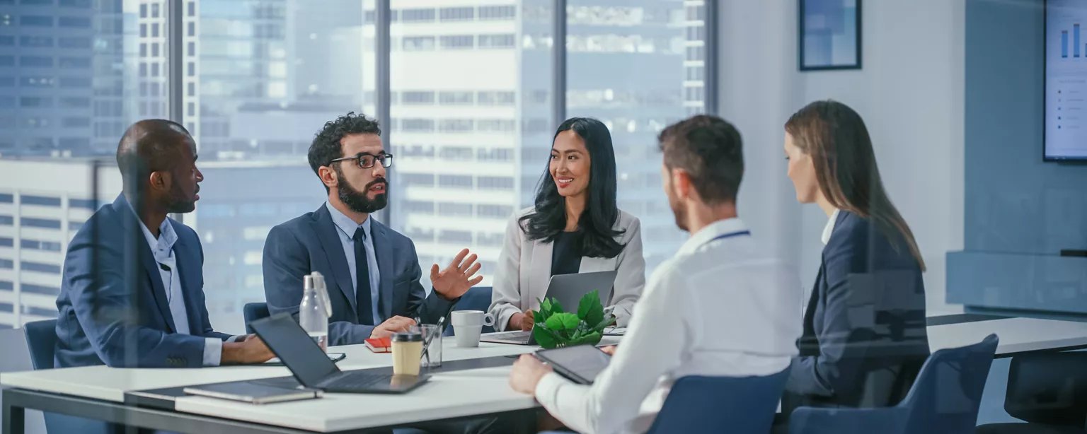 A group of executives sit at a table in a conference room discussing governance, risk and compliance issues - an example of cross-functional collaboration on GRC.