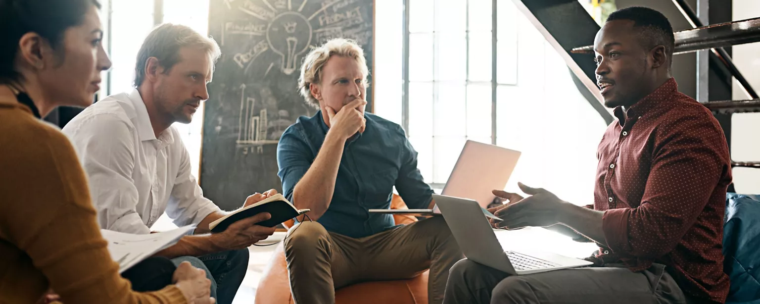 Four employees of a small business sit in chairs and discuss ideas in an informal brainstorming session.