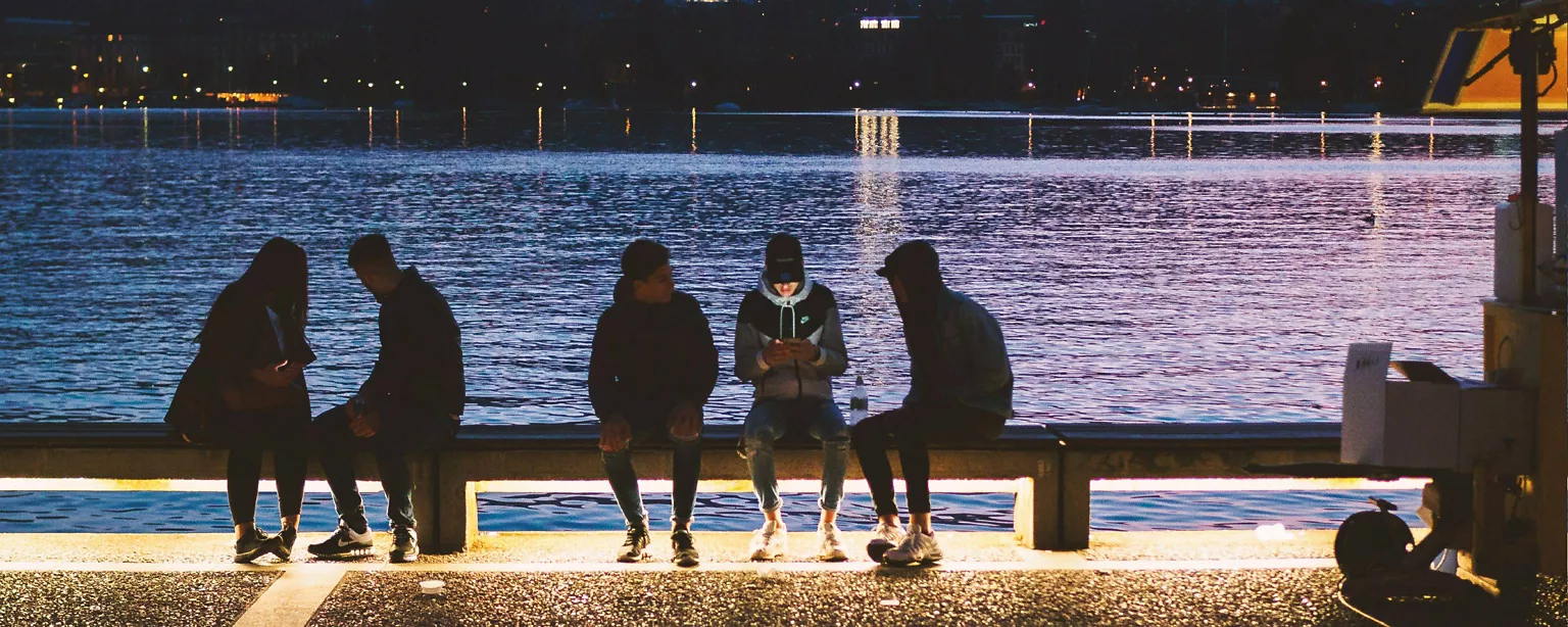 Junge Menschen sitzen am Abend auf einer Begrenzung an einem See