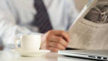 Coffee cup, laptop, and newspaper