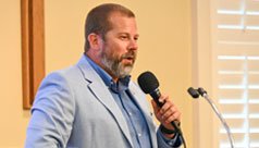 Guy in a blue sport coat speaking with a microphone at a podium