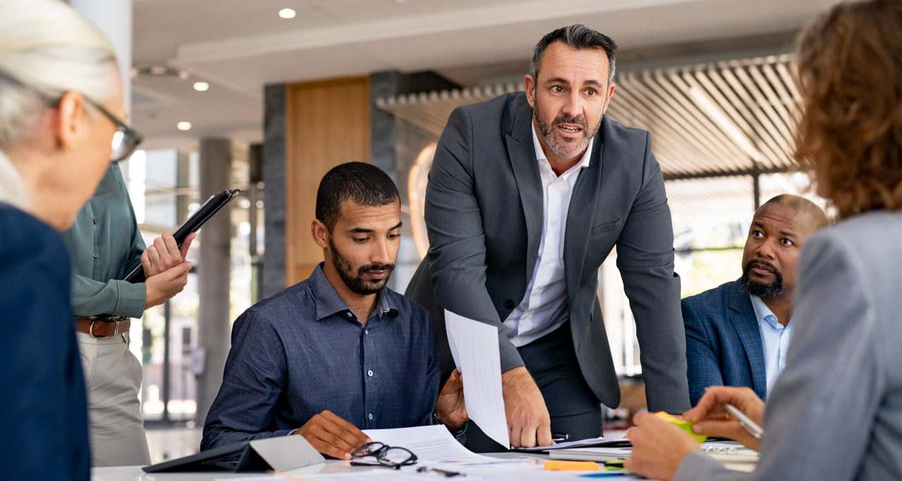 businesswoman holding tablet in front of coworkers working at their desks