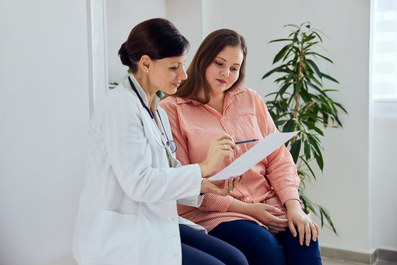 woman sitting with health care practitioner reviewing notes on a clipboard