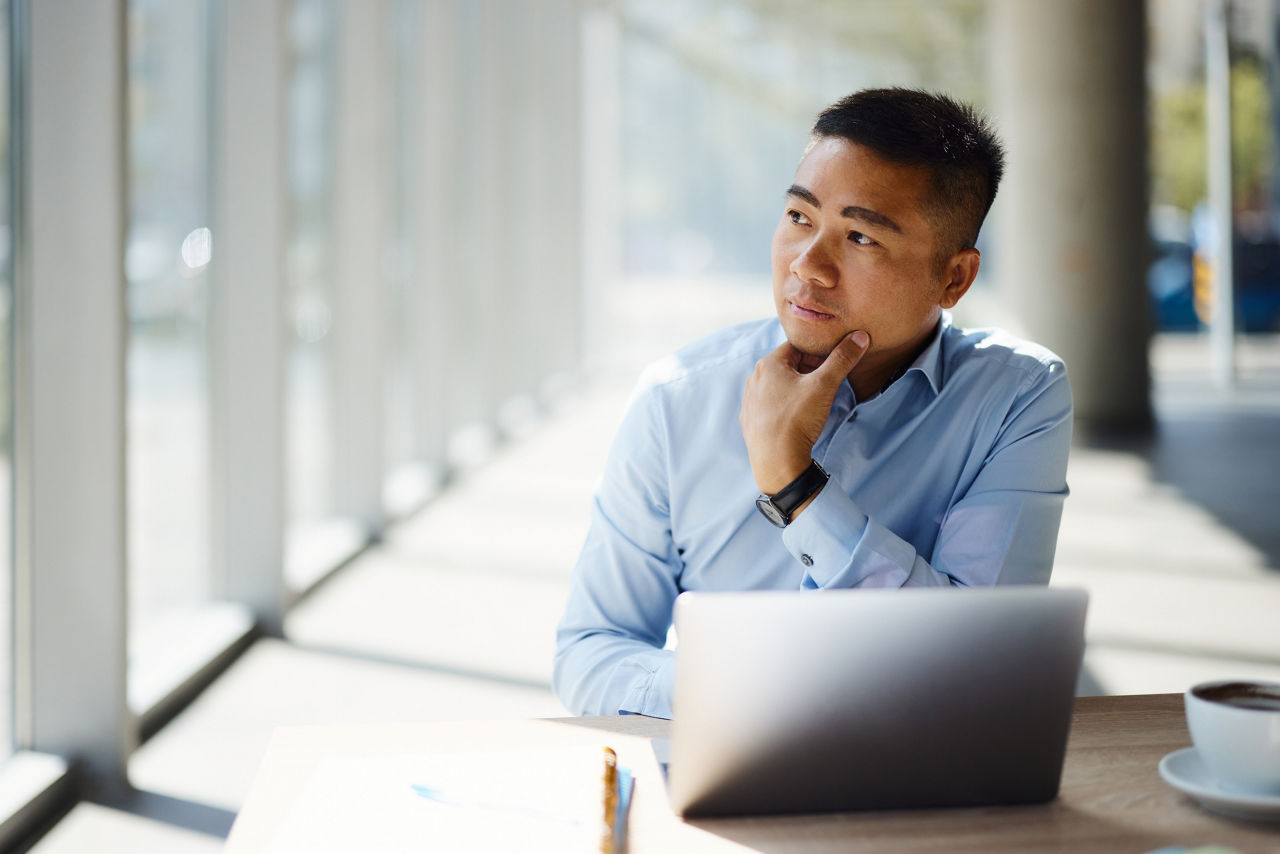 A man sitting in front of a laptop looking out the window