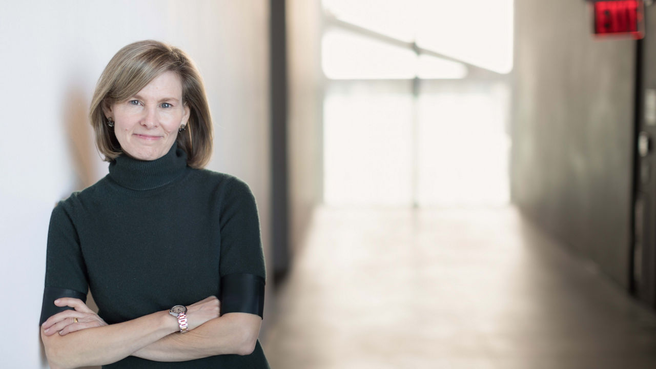 A woman leaning against a wall with her arms crossed.