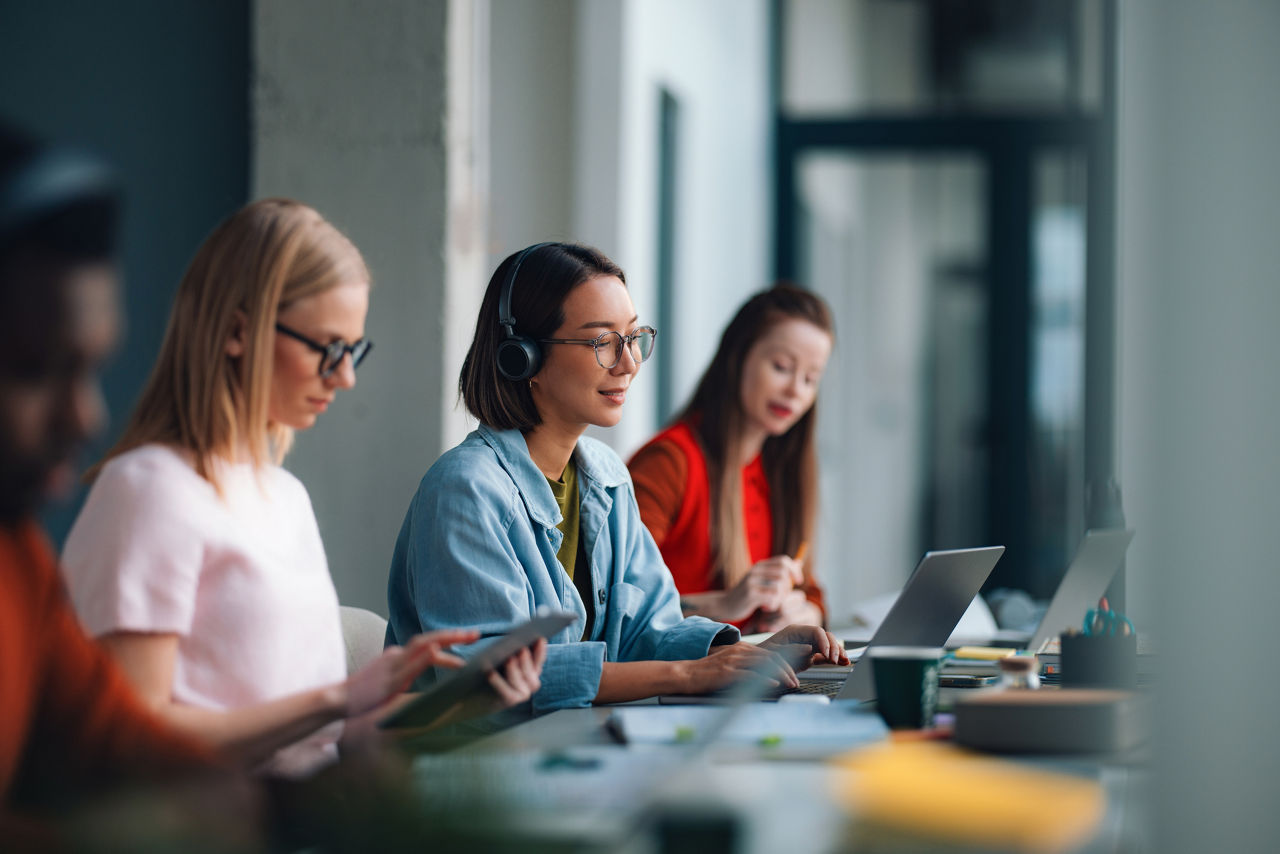 three people sitting in a row looking at laptops or paper while studying