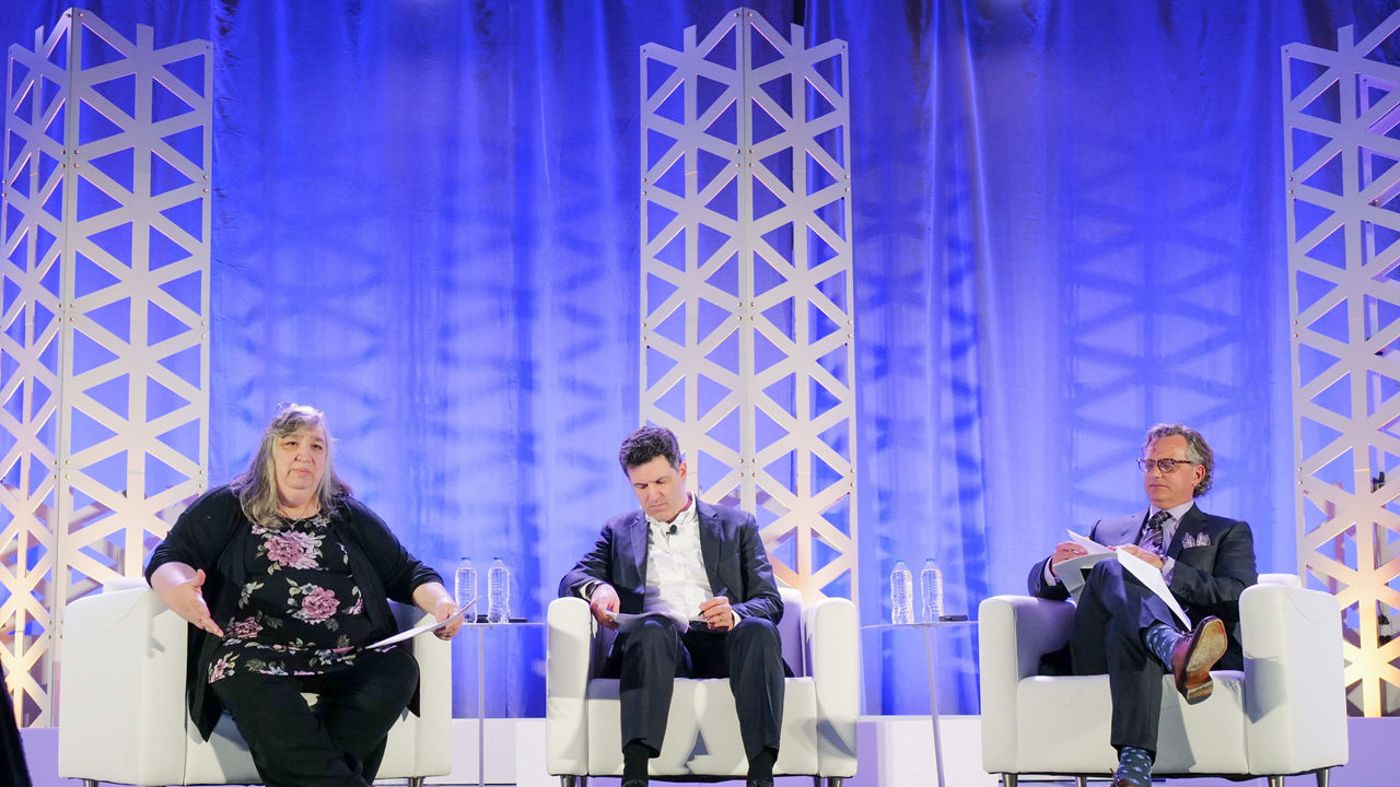 Three people sitting on chairs on a stage.