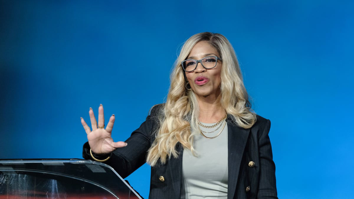 A woman wearing glasses and a suit giving a speech.