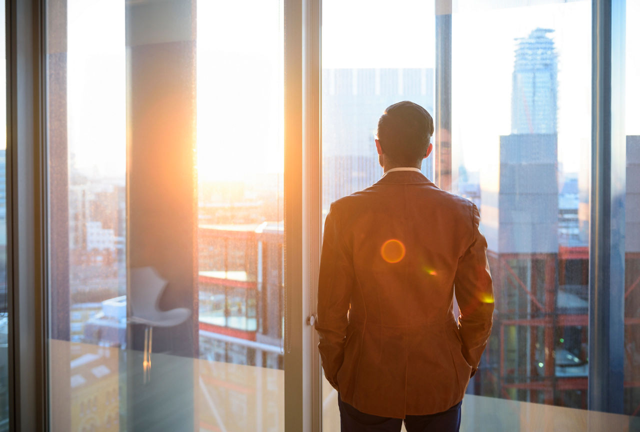 a man facing the window of an office building looking at the sunrise