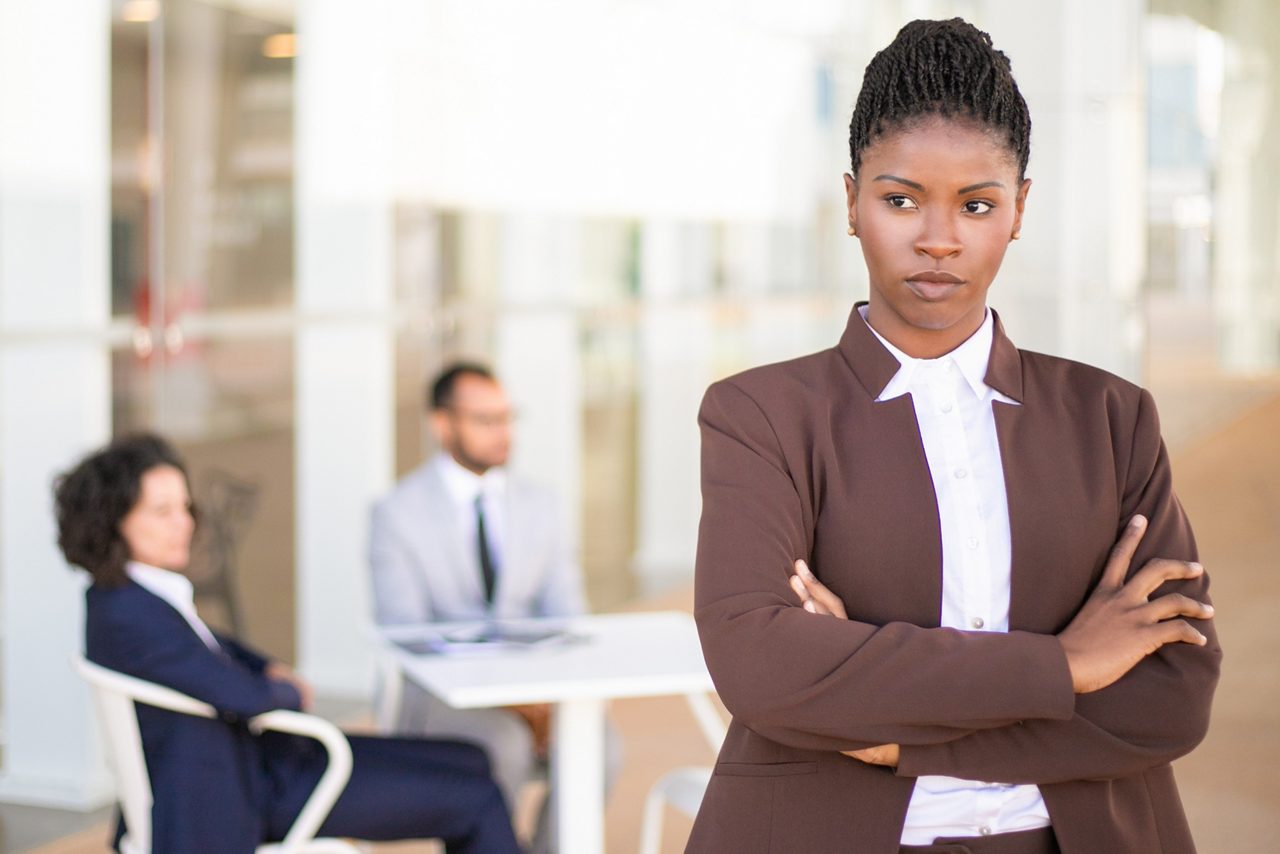 Woman with arms crossed by coworkers