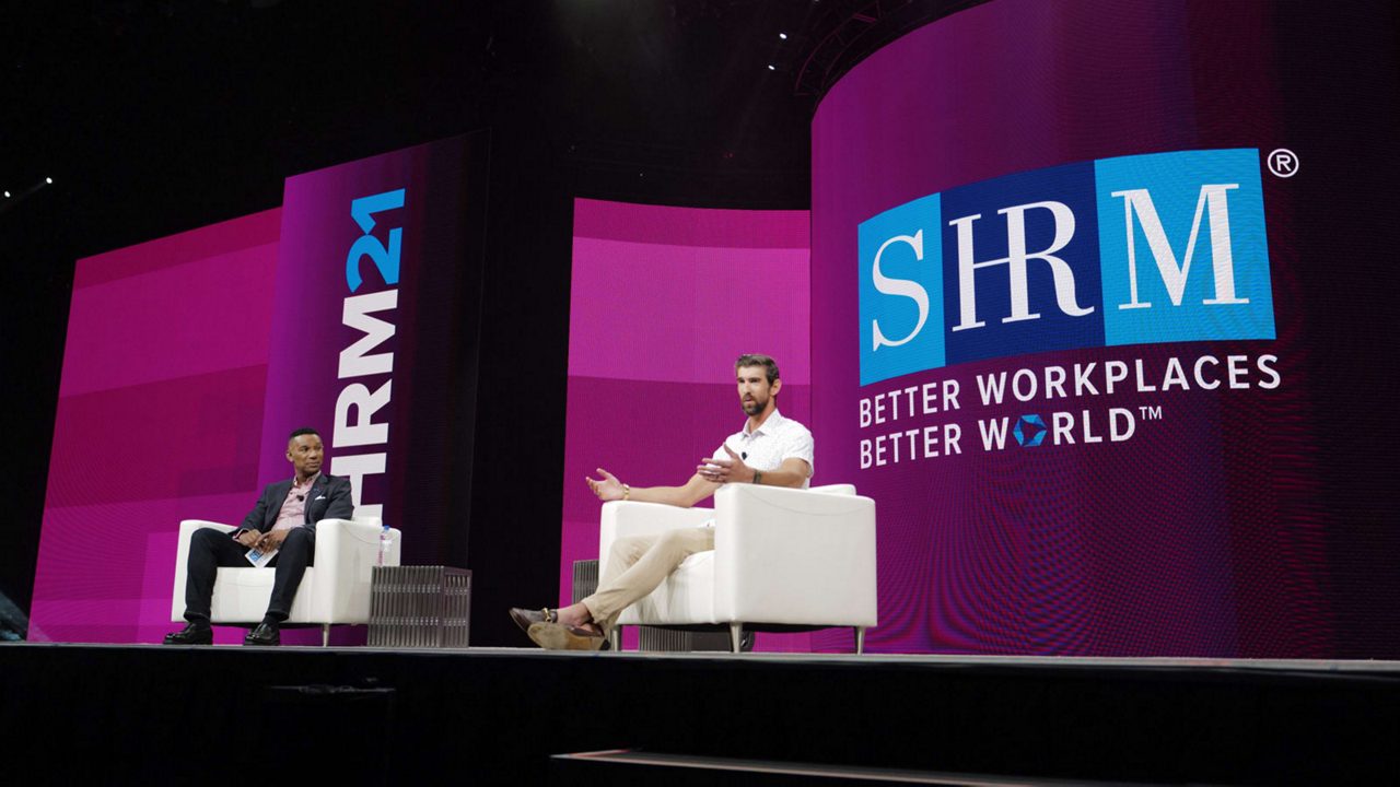 Johnny C. Taylor Jr. and Michael Phelps sitting in chairs on stage at the SHRM conference.