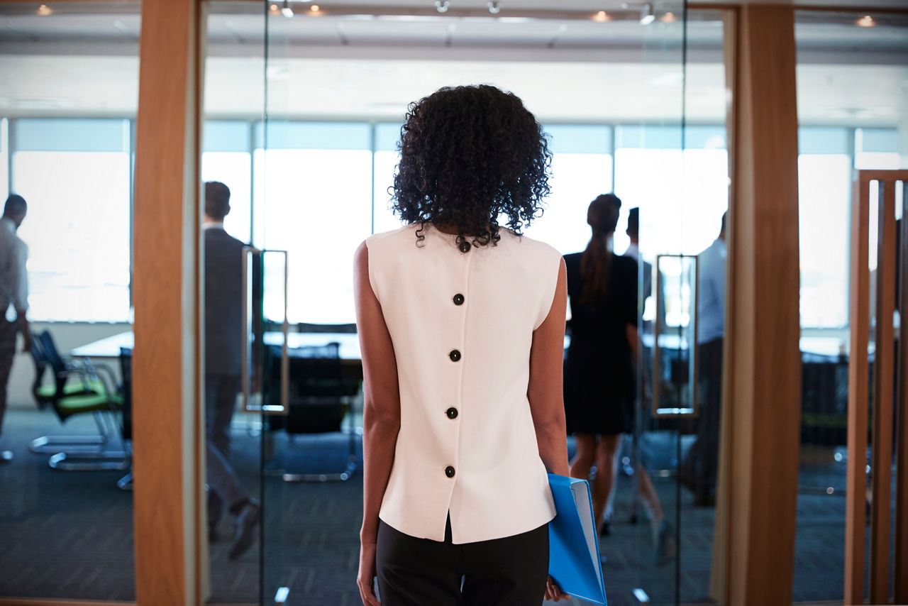 A view of the back of a woman about to enter a boardroom with people inside