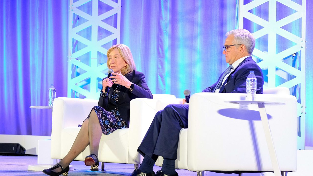 A man and woman sitting on chairs at a conference.