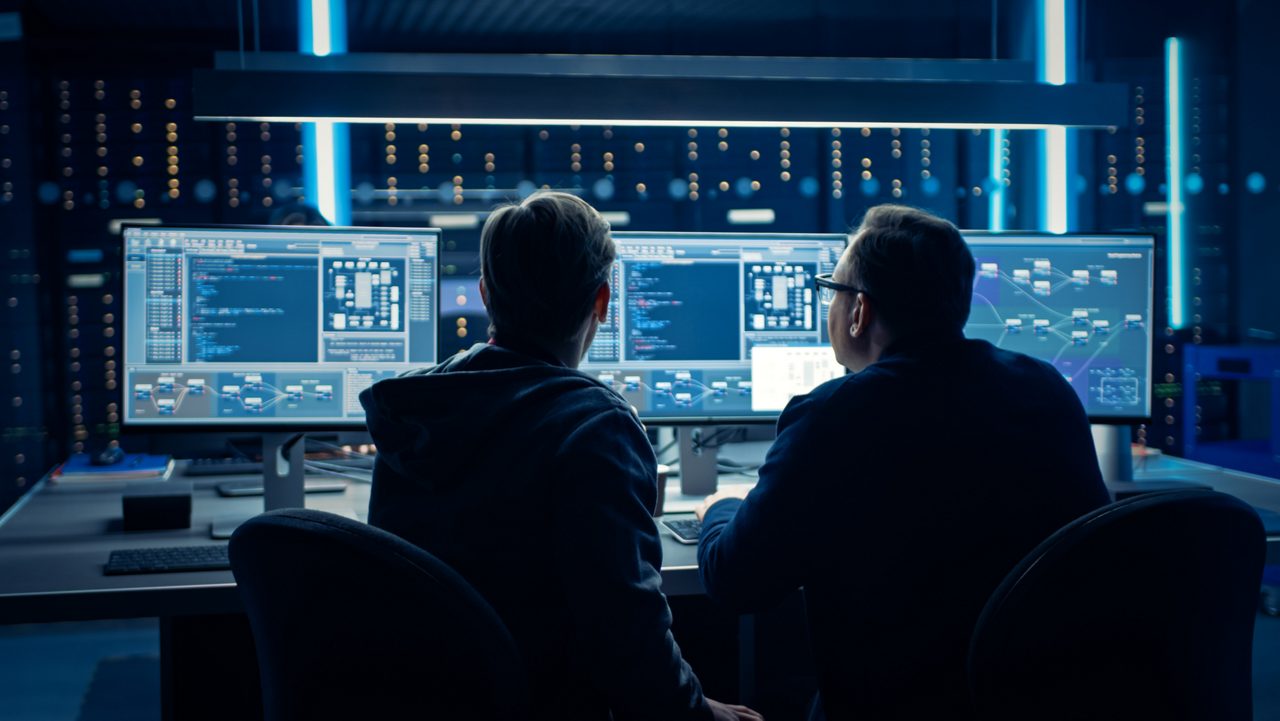 Two people sit in front of computer screens, working together on problem