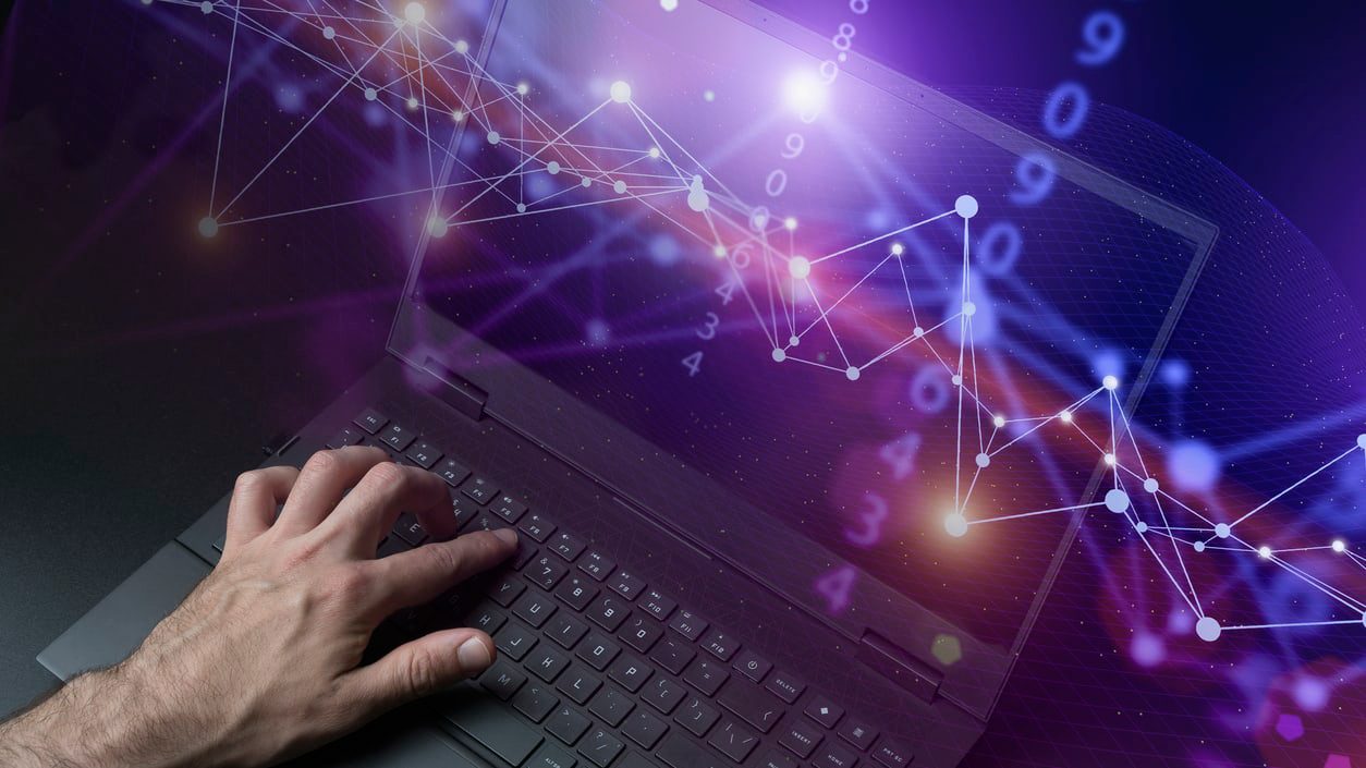 A man is typing on a laptop with a purple background.