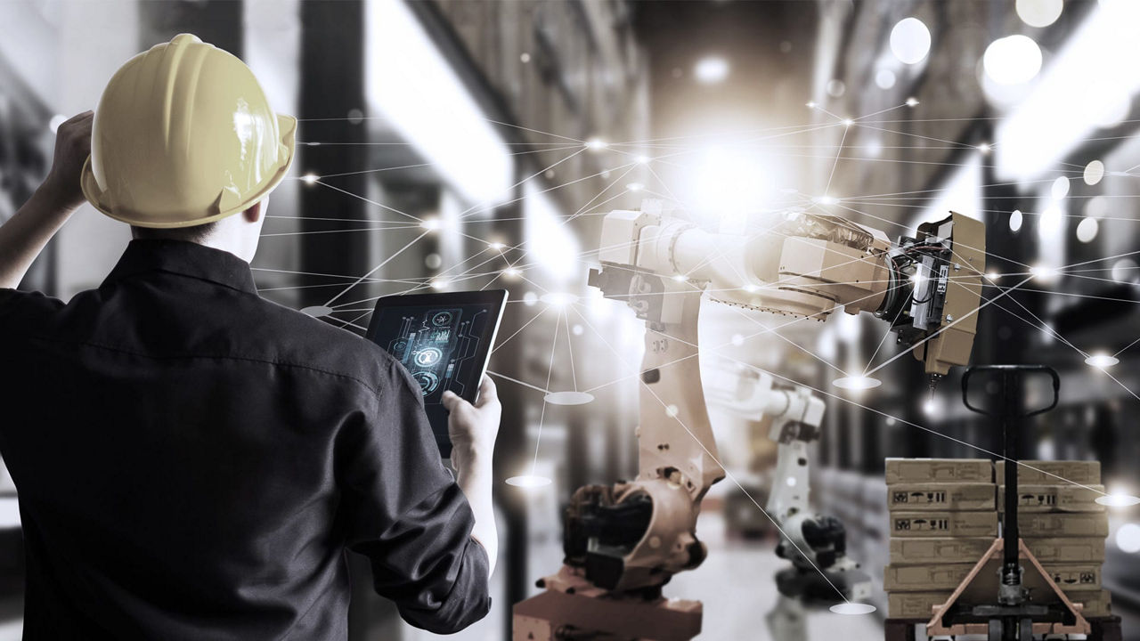 A man in a hard hat is looking at a tablet in a warehouse.