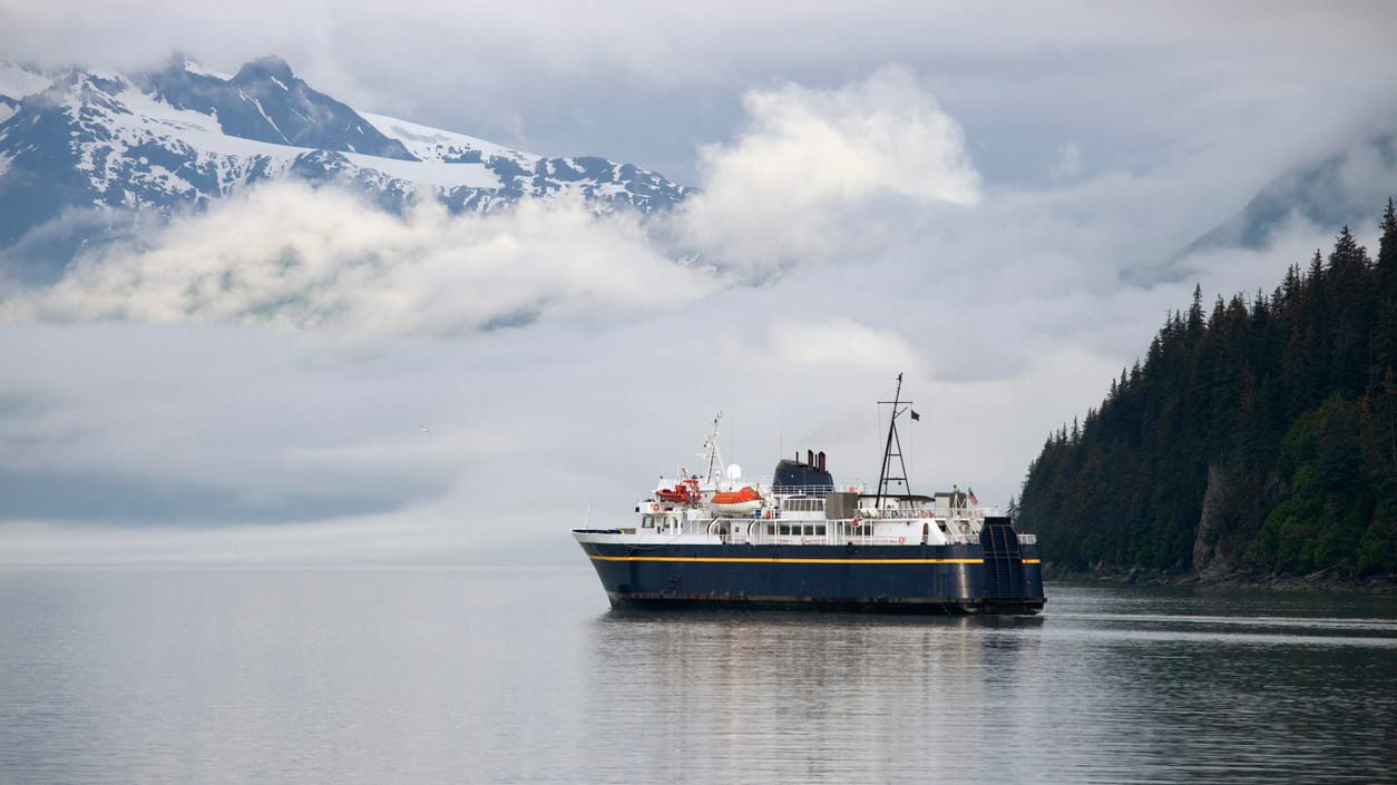 A ferry boat in the middle of a body of water with mountains in the background.