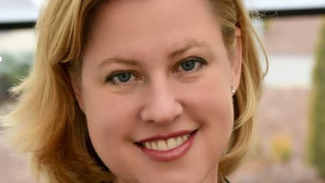 A woman in a business suit smiling in front of a window.