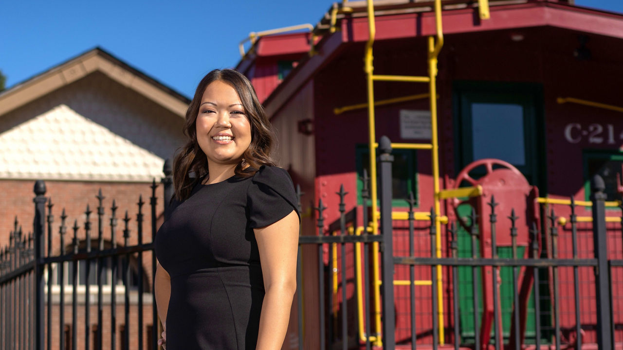 A woman in a black dress standing in front of a train car.