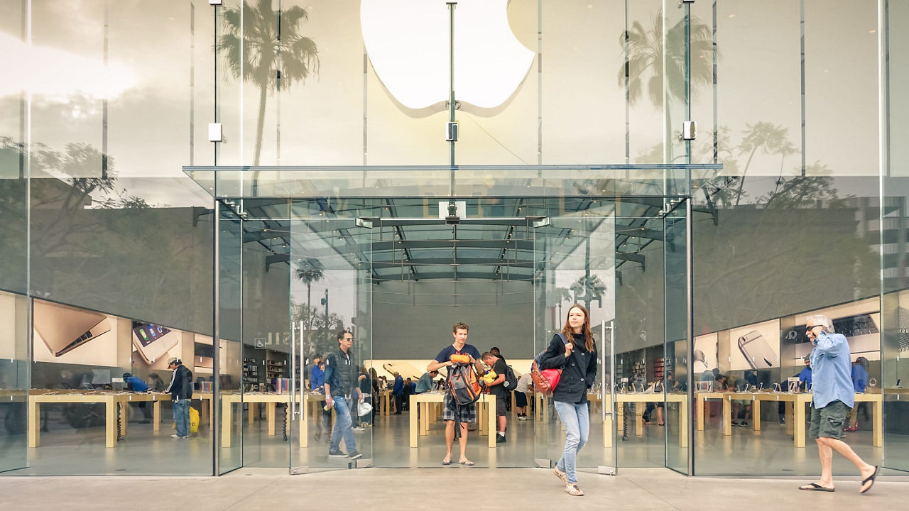 A group of people walking in front of an apple store.