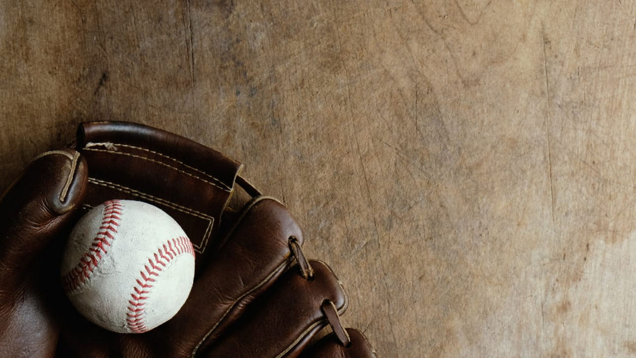 A baseball in a leather glove on a wooden table.