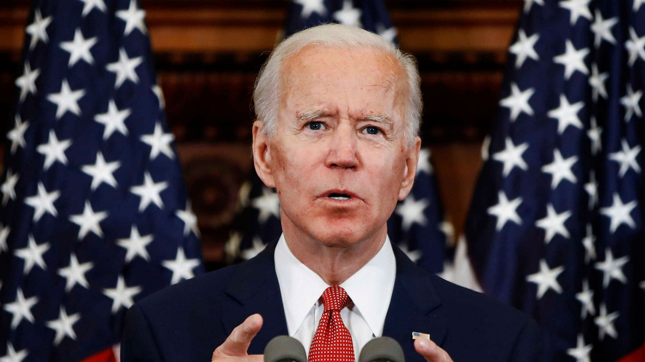 Joe biden gives a speech in front of american flags.