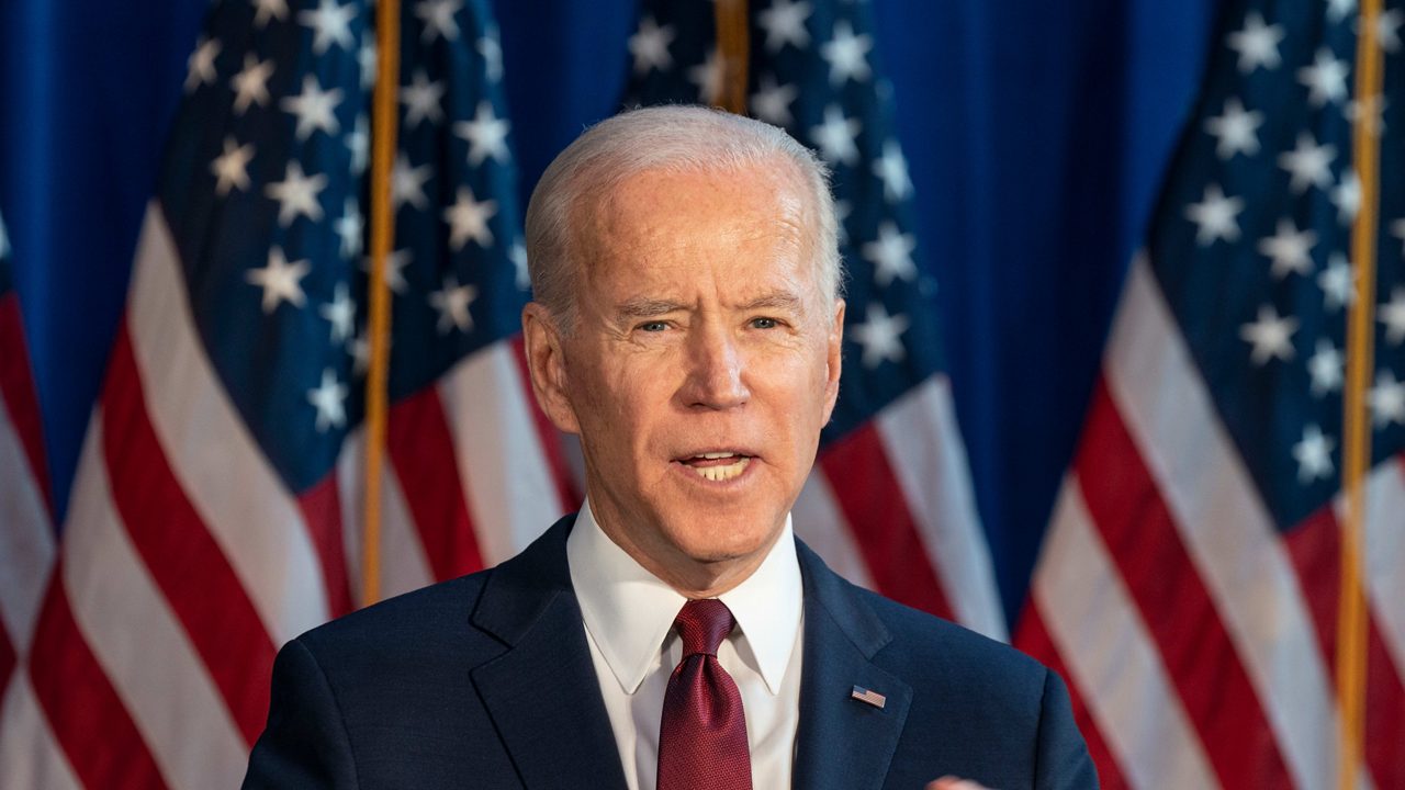 Joe biden speaks at a podium in front of american flags.