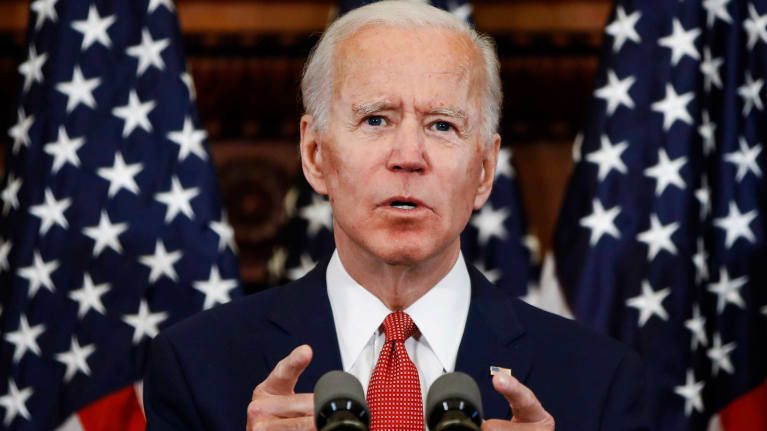 Joe biden speaks at a podium in front of american flags.