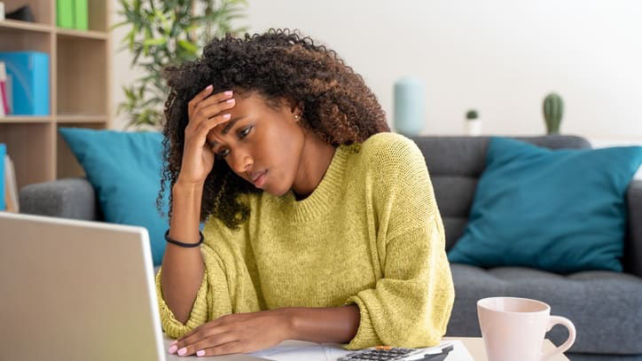 A woman is sitting at her computer with her head in her hands.