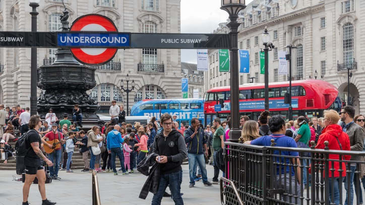 A crowd of people standing near a red double decker bus in london.