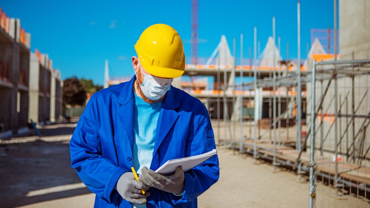 A construction worker wearing a helmet and hard hat is holding a clipboard.