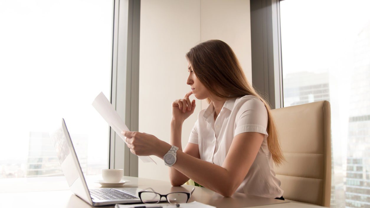 A woman sitting at a desk with a laptop in front of a window.