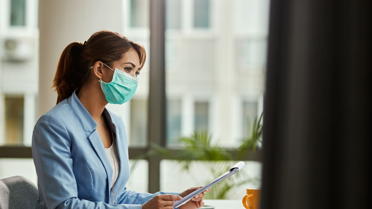 A woman wearing a surgical mask at her desk.