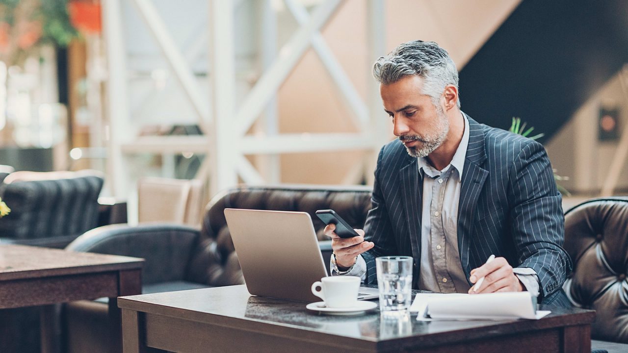 A man in a suit sitting at a table with a laptop and a cup of coffee.