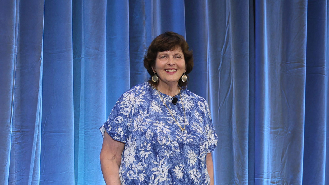 A woman in a blue dress standing in front of a curtain.