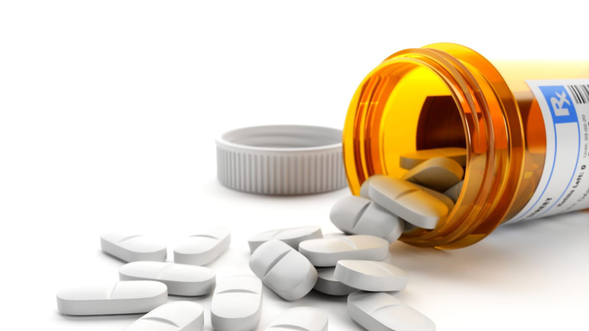 A pill bottle with pills spilling out on a white background.