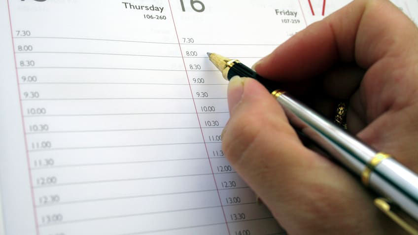 A person writing on a calendar with a pen.
