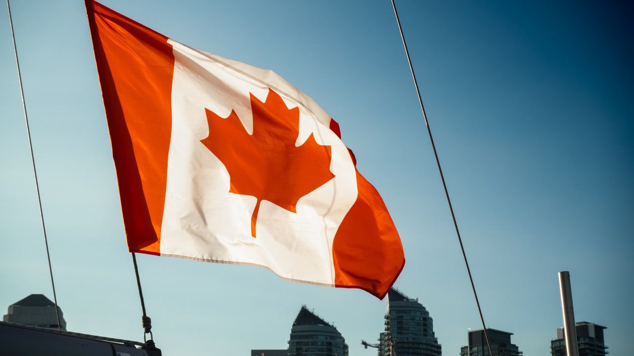 A canadian flag flies on a boat in front of a city.