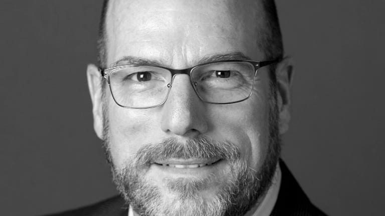 A black and white photo of a bald man in a suit and tie.