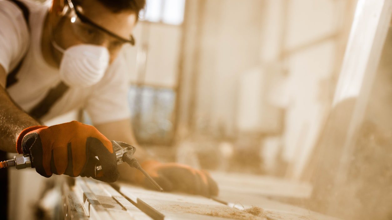 A man wearing a mask and gloves is sanding a piece of wood.