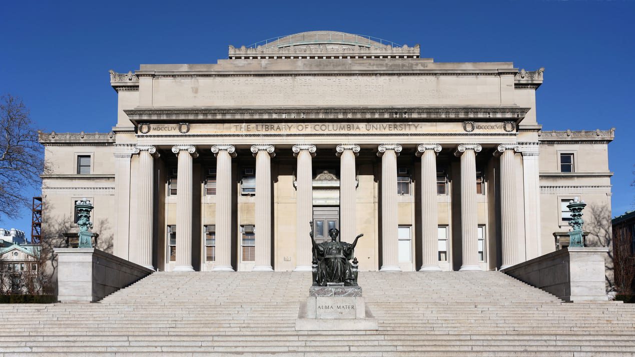 A large building with columns and a statue on the steps.