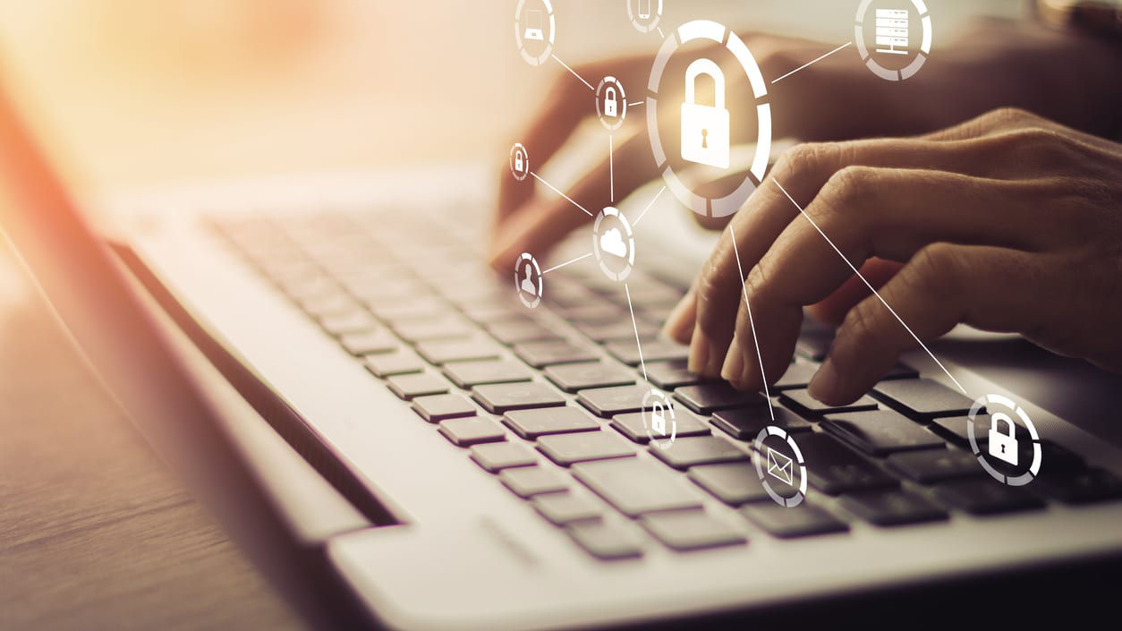 A person typing on a laptop with security icons on it.