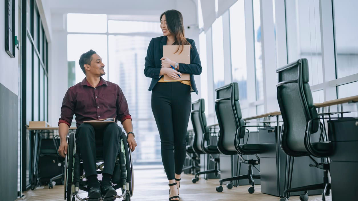 A man in a wheelchair is talking with a woman in an office.