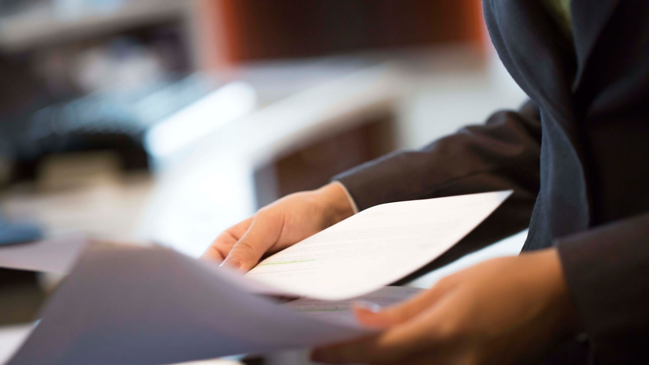 A business woman is holding a piece of paper in front of a computer.