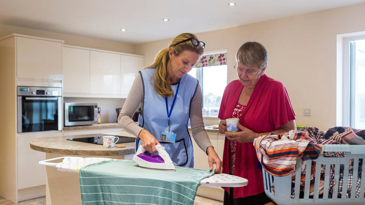 Two women ironing clothes in a kitchen.