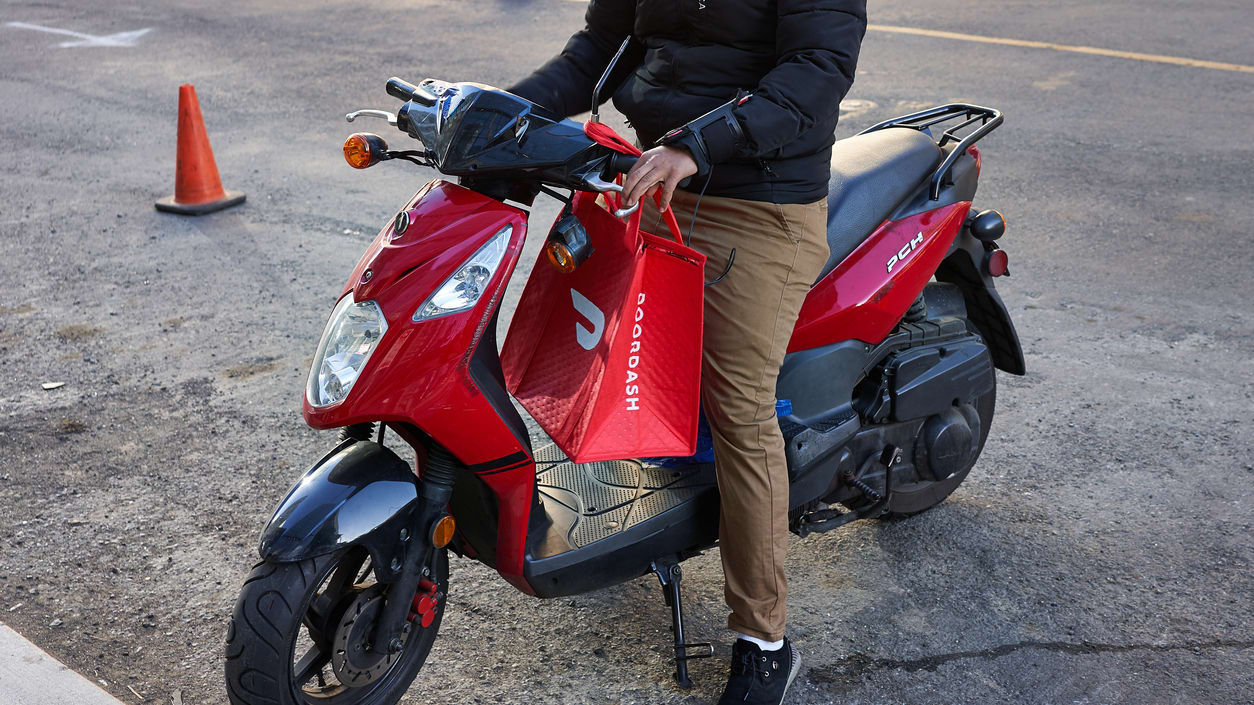A man riding a red scooter with a shopping bag.