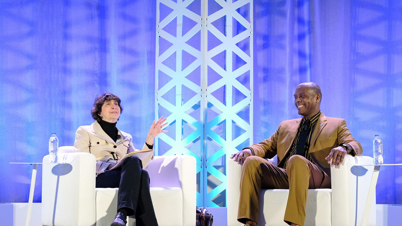 A man and woman sitting in chairs on a stage.