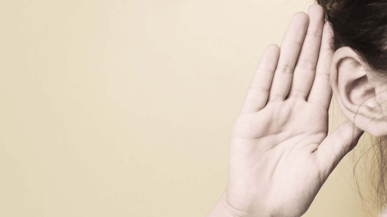 A woman is holding her hand up to her ear.