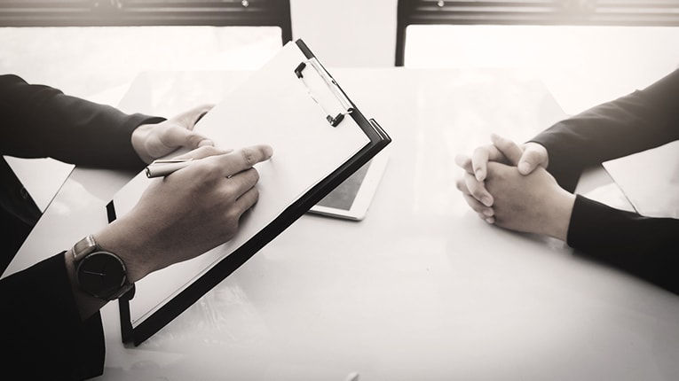 Two business people sitting at a table and holding a clipboard.